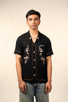 Man wearing a black short sleeve embroidered streetwear shirt with white buttons and jeans