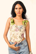 Woman wearing a floral print top with green ribbon straps and light blue jeans, streetwear style