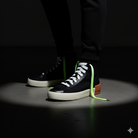 Black high top shoes and the shoelaces worn are Neon green and white gradient shoelaces on a shadow background 
