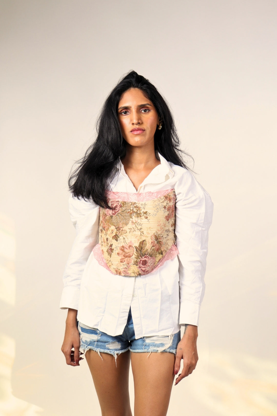 Woman wearing floral corset over white shirt and denim shorts, streetwear fashion