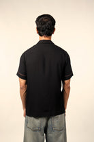 Man wearing black short sleeve shirt and blue jeans, viewed from the back