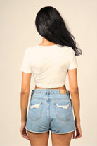 Woman wearing a white crop top and distressed high-waisted denim shorts, back view