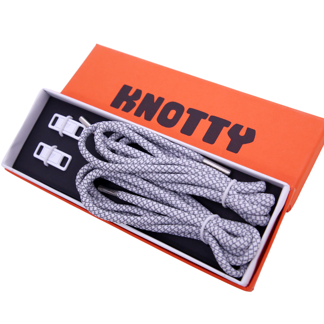 A set of reflective shoelaces and a premium metal dubrae tag with the brand name 'KNOTTY' on a orange and black label packaging.