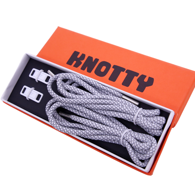 A set of reflective shoelaces and a premium metal dubrae tag with the brand name 'KNOTTY' on a orange and black label packaging.