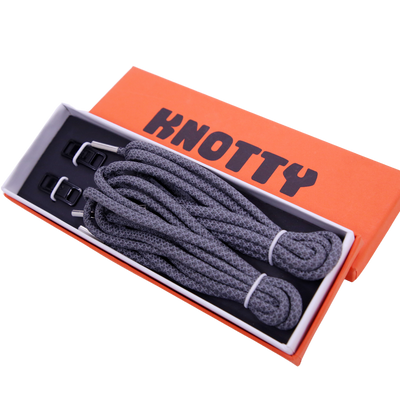 A set of reflective shoelaces and a premium metal dubrae tag, packaged together with the brand name 'KNOTTY' printed on an orange and black box.