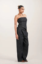 Woman wearing strapless dark denim jumpsuit with wide-leg pants and brown shoes in studio