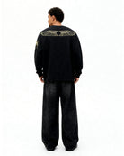 Person wearing a black outfit with gold screen print on the back against a white background