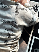 Person wearing light gray sweater with black broken chain graphic design lying on patterned carpet