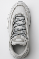 White sneaker with white reflective laces on a light gray background