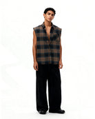 Man wearing a plaid sleeveless shirt and black pants on a white background